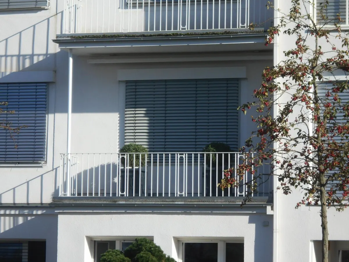 Façade blanche d'immeuble à balcons et garde-corps blancs, volets roulants gris à demi baissés sur les baies